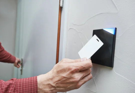 A hand taps a magnetic keycard against a digital master key system