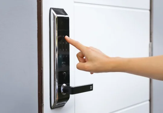 A hand presses keys on an electric keypad above a door handle